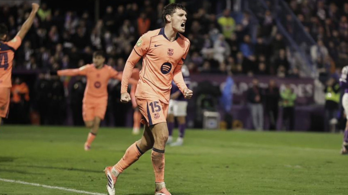 A focused footballer, wearing a blue and red jersey, stands on a pitch with dramatic lighting.