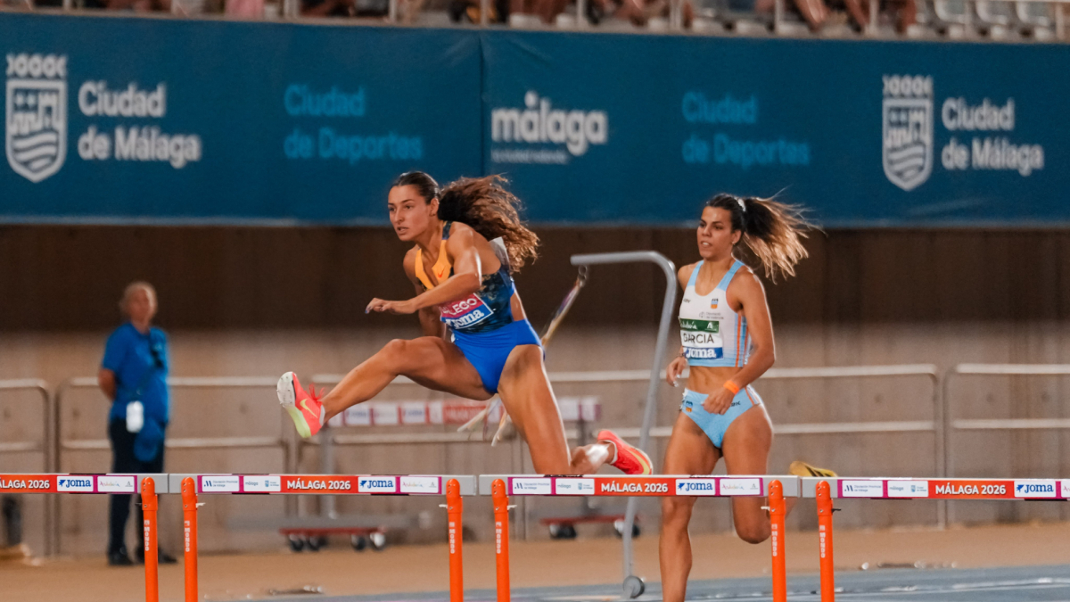 Sara Gallego corre in pista con un'espressione di soddisfazione dopo un'ottima prestazione, con il cronometro che segna un tempo competitivo