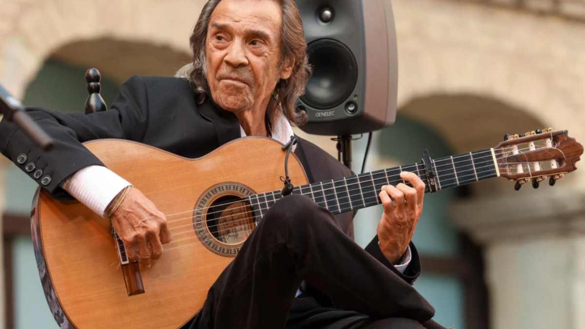Un uomo suona la chitarra flamenca in un palcoscenico, mentre un pubblico lo osserva con attenzione