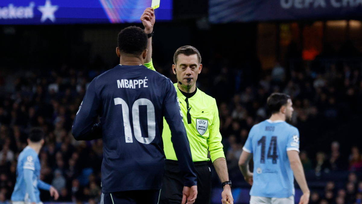 Giocatori e squadre in campo durante una partita di Champions League, con un arbitro che mostra un cartellino giallo