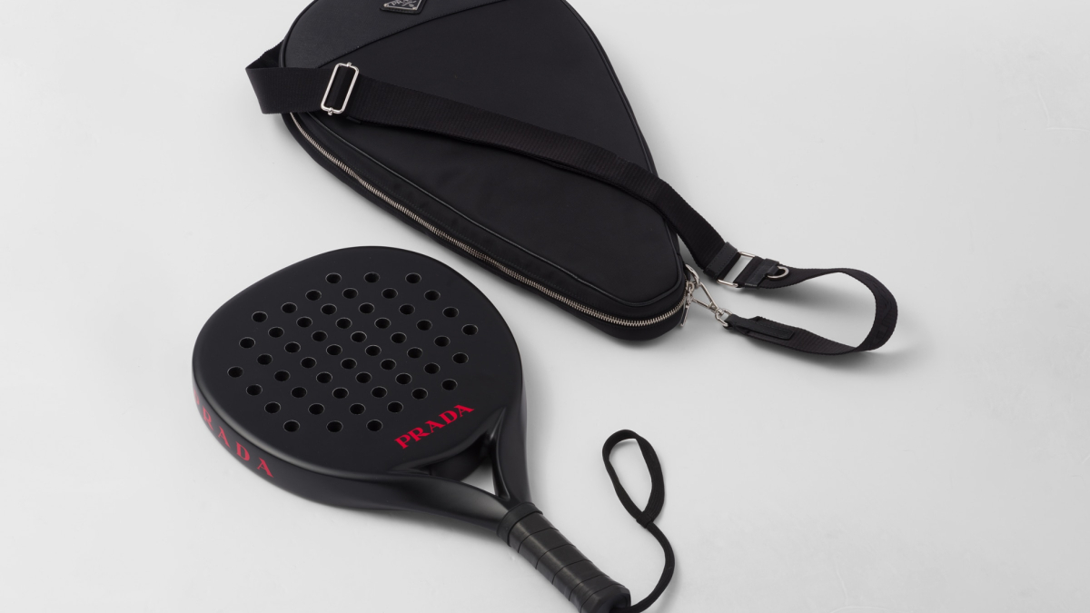 Una pala da pádel di Prada in nero con logo rosso, posata su un fondo neutro