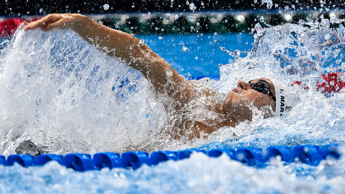 Atleta spagnolo nuota in una piscina, con spettatori intorno, in una competizione internazionale