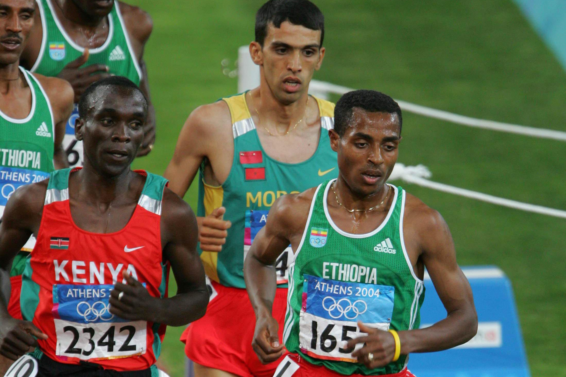Eliud Kipchoge y Kenenisa Bekele, con Hicham El Guerrouj de fondo, en la final de los 5.000 metros de los Juegos de Atenas de 2004.