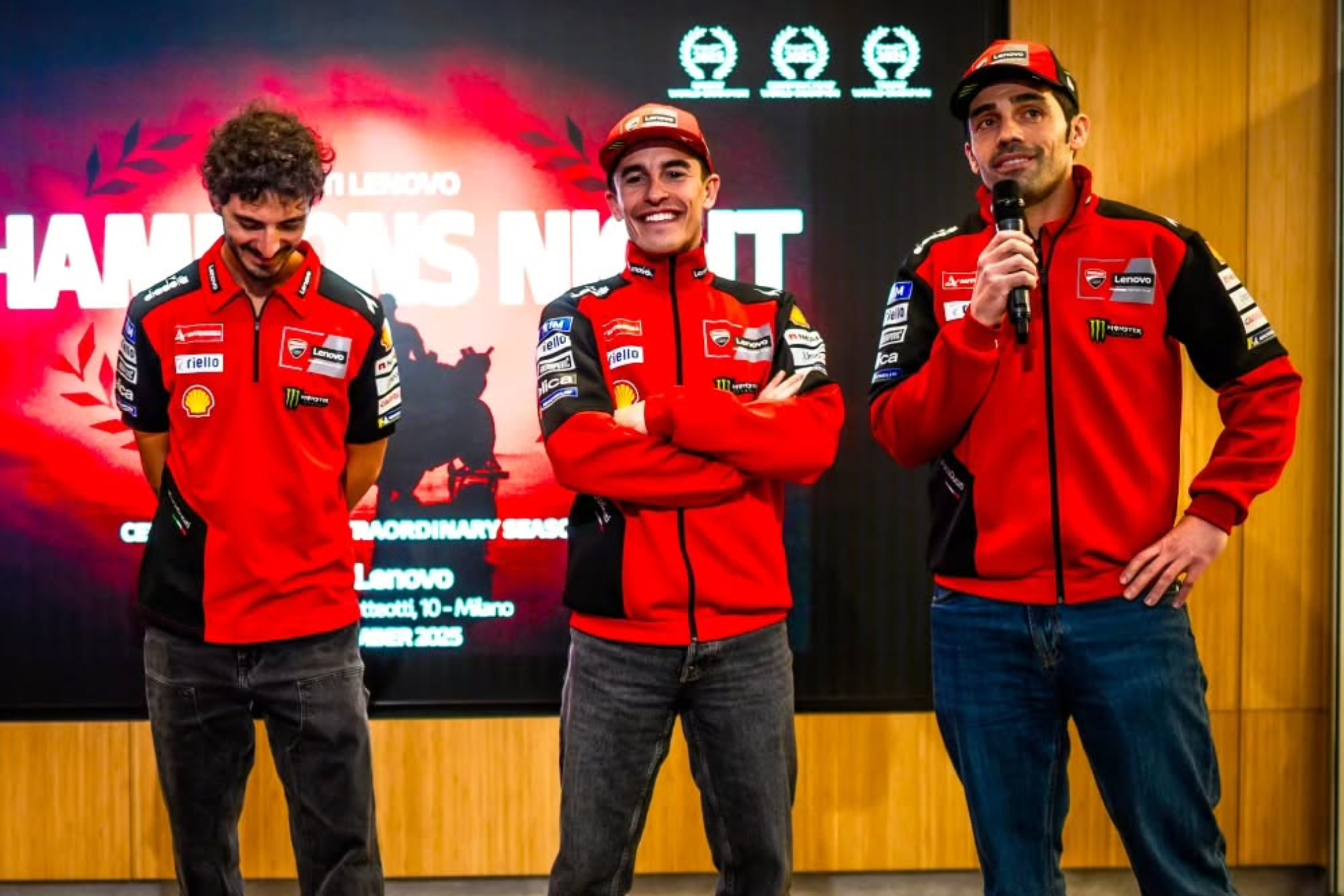 Pirro, con el micrófono en la mano diestra, habla delante de Marc y Pecco.