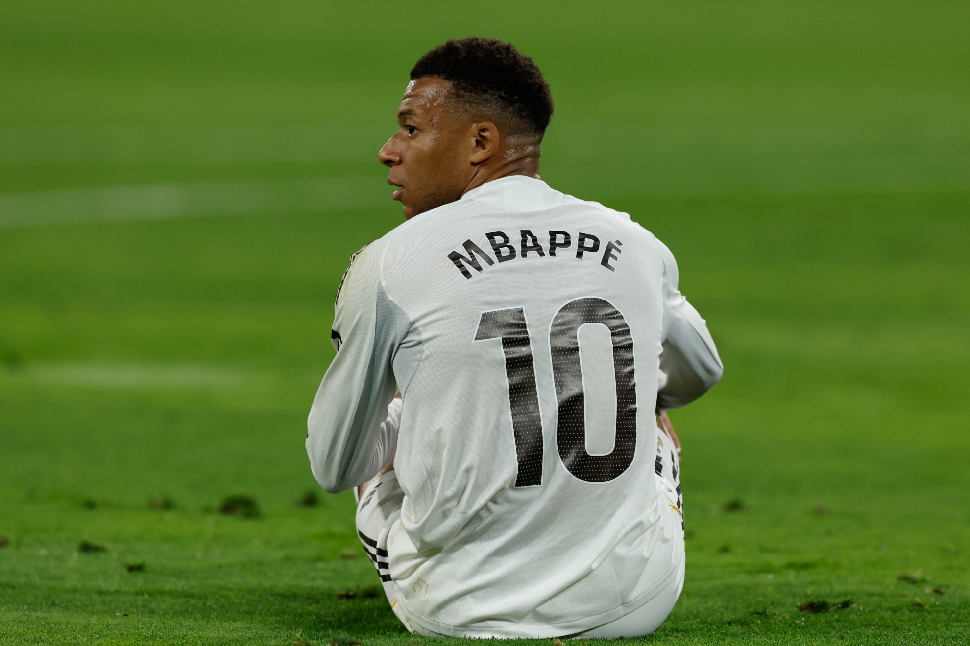 Mbappé, sentado en el césped durante un partido con gesto serio.