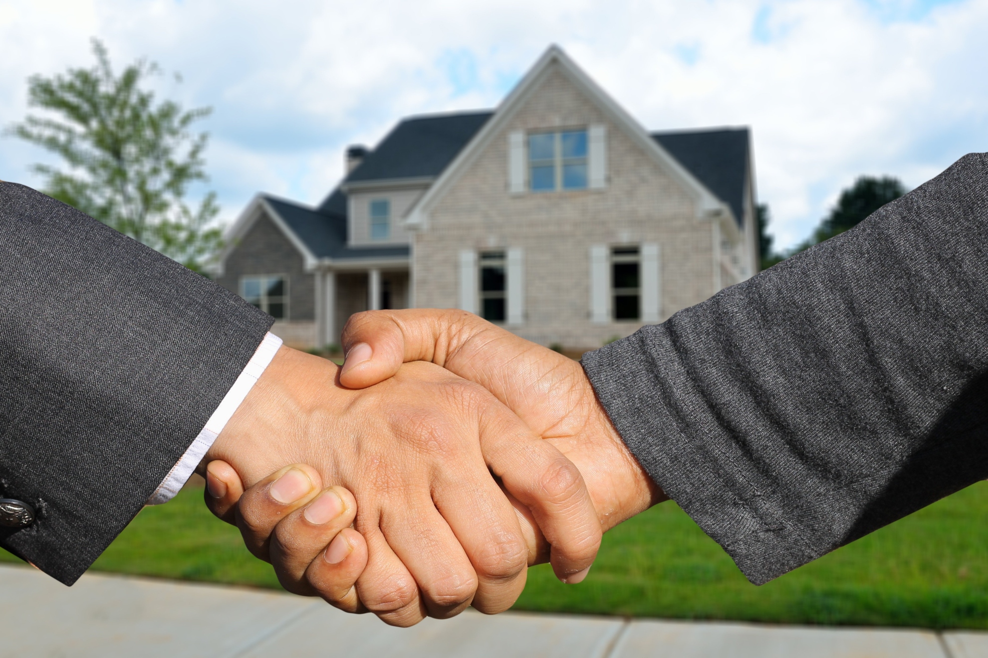 Imagen de recurso de dos personas dándose la mano y, al fondo, una vivienda.