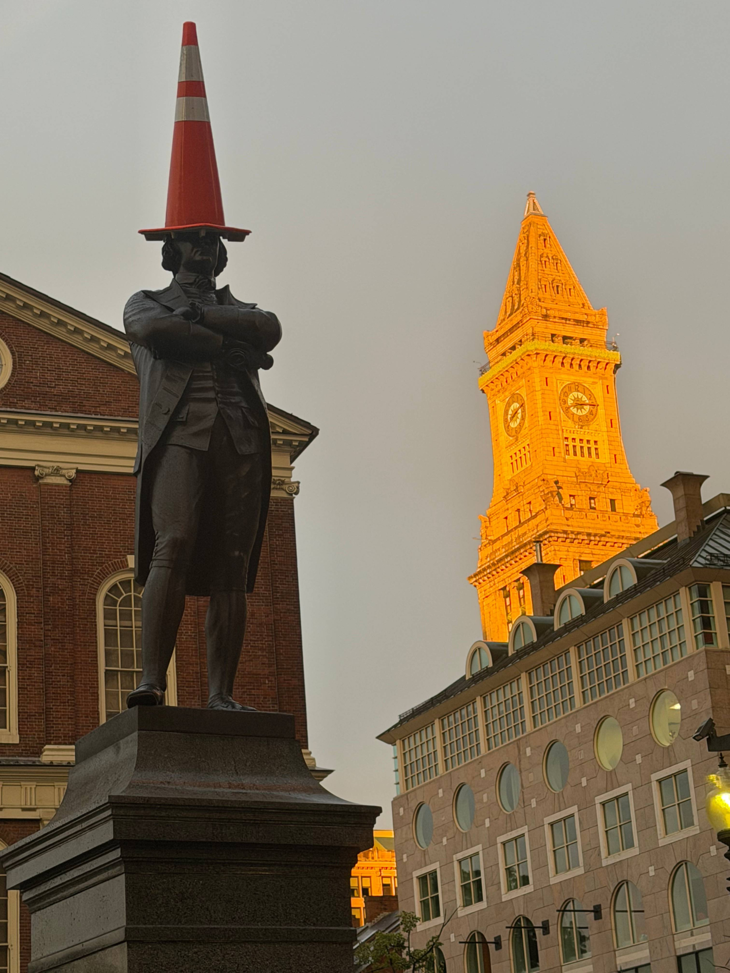 A cone on a statue of Samuel Adams with the Custom House Tower in the background.