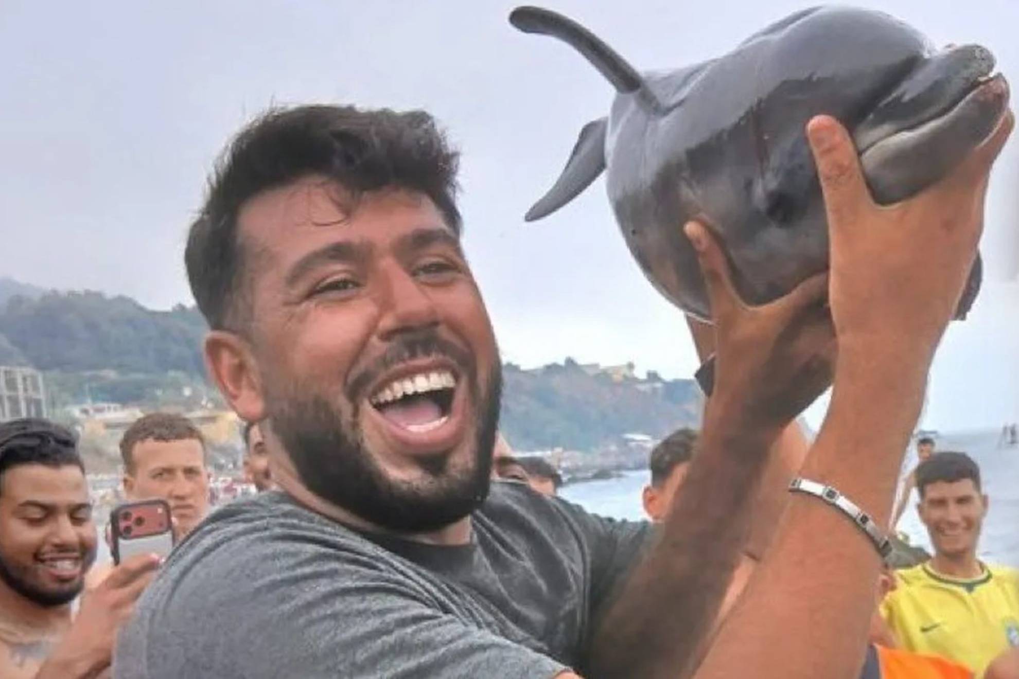 Un inmigrante sostiene a la cría de delfín. RRSS