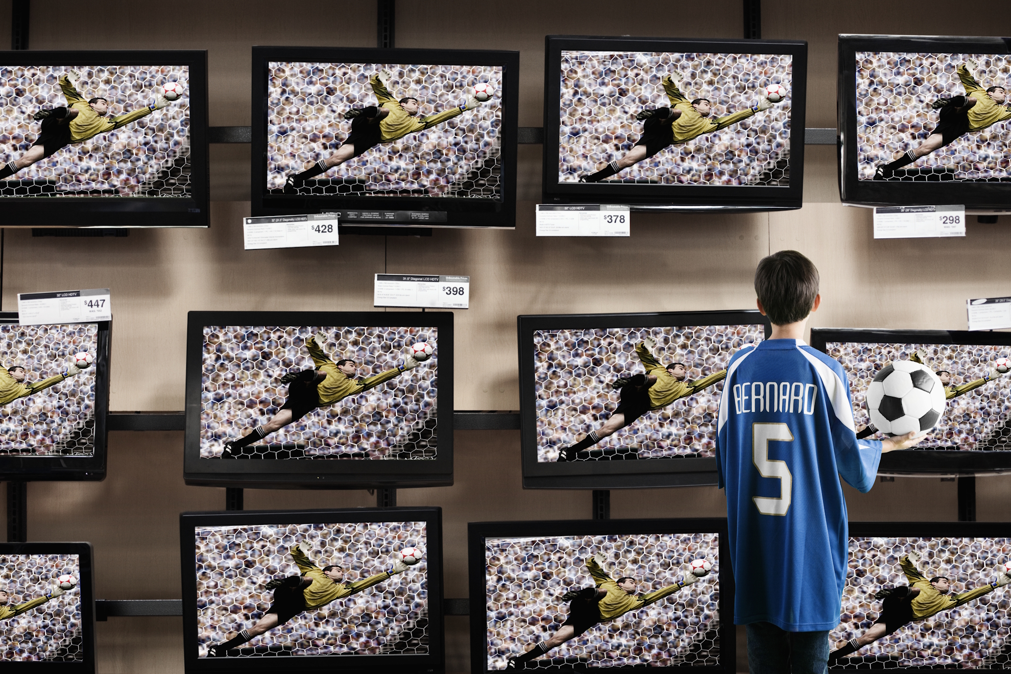 Un niño con un balón observa televisores en una tienda. Getty