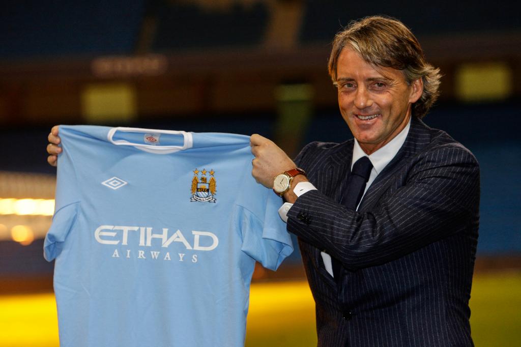 El técnico Robert Mancini alza una camiseta del Manchester City, el 21 de diciembre de 2009. (AP Foto/Jon Super)