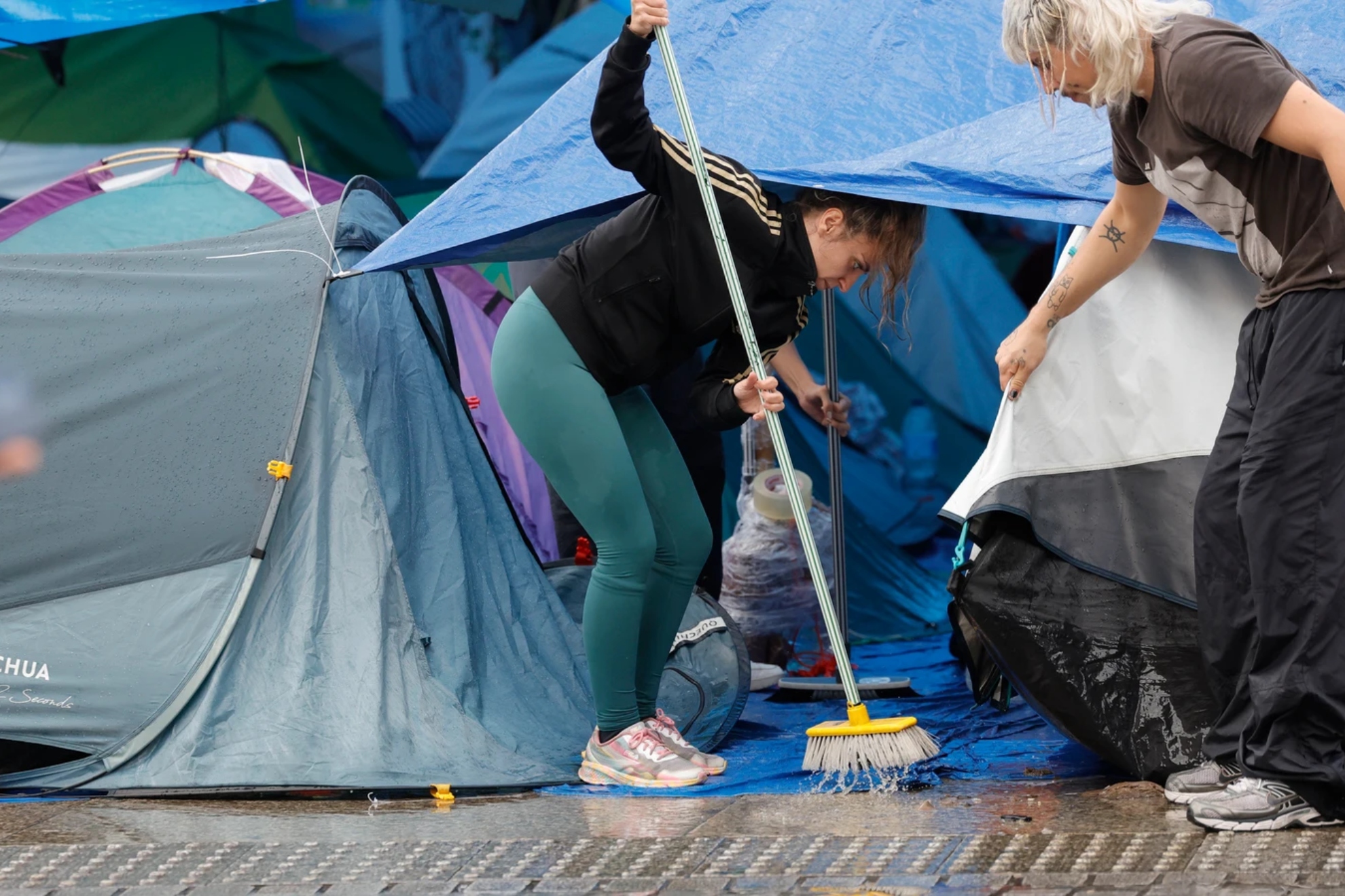 Imagen de varias personas retirando agua de la acampada en la Puerta del Sol. EFE